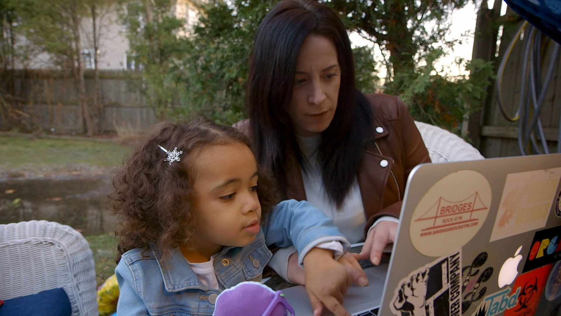 Justice Through Code graduates coding on a laptop outside with a young child.