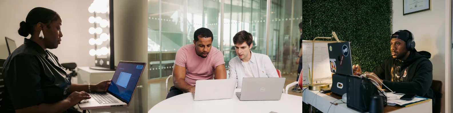 Fair Chance Futures students collaborating in a modern office space. A woman works on a laptop on the left, while in the center two men - a JTC student and his MBA student advisor - work together at laptops around a white table. On the right, another person works at a desk with multiple monitors. The bright, contemporary workspace features floor-to-ceiling windows and a living wall backdrop.