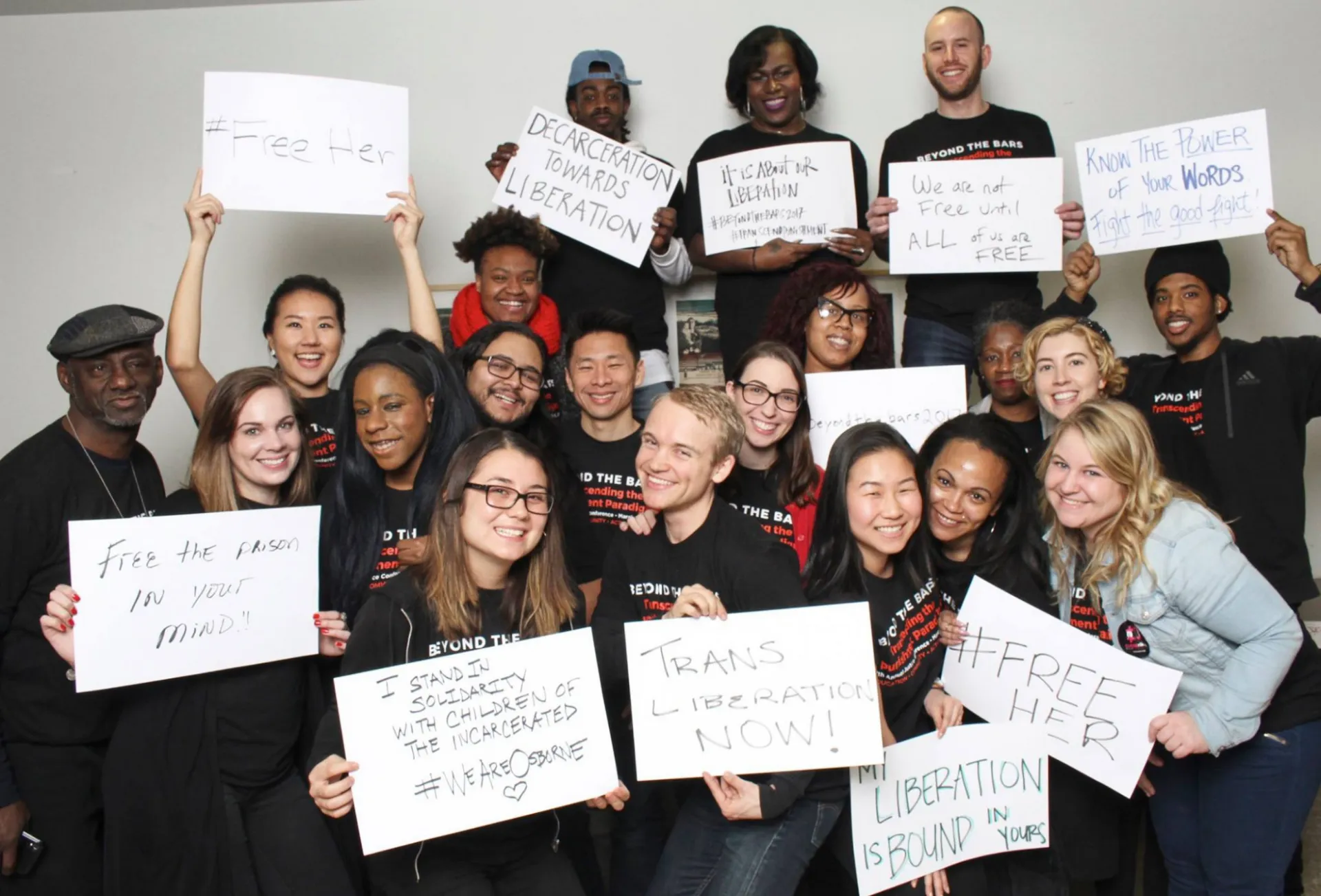 Group photo of people in black shirts holding up white signs