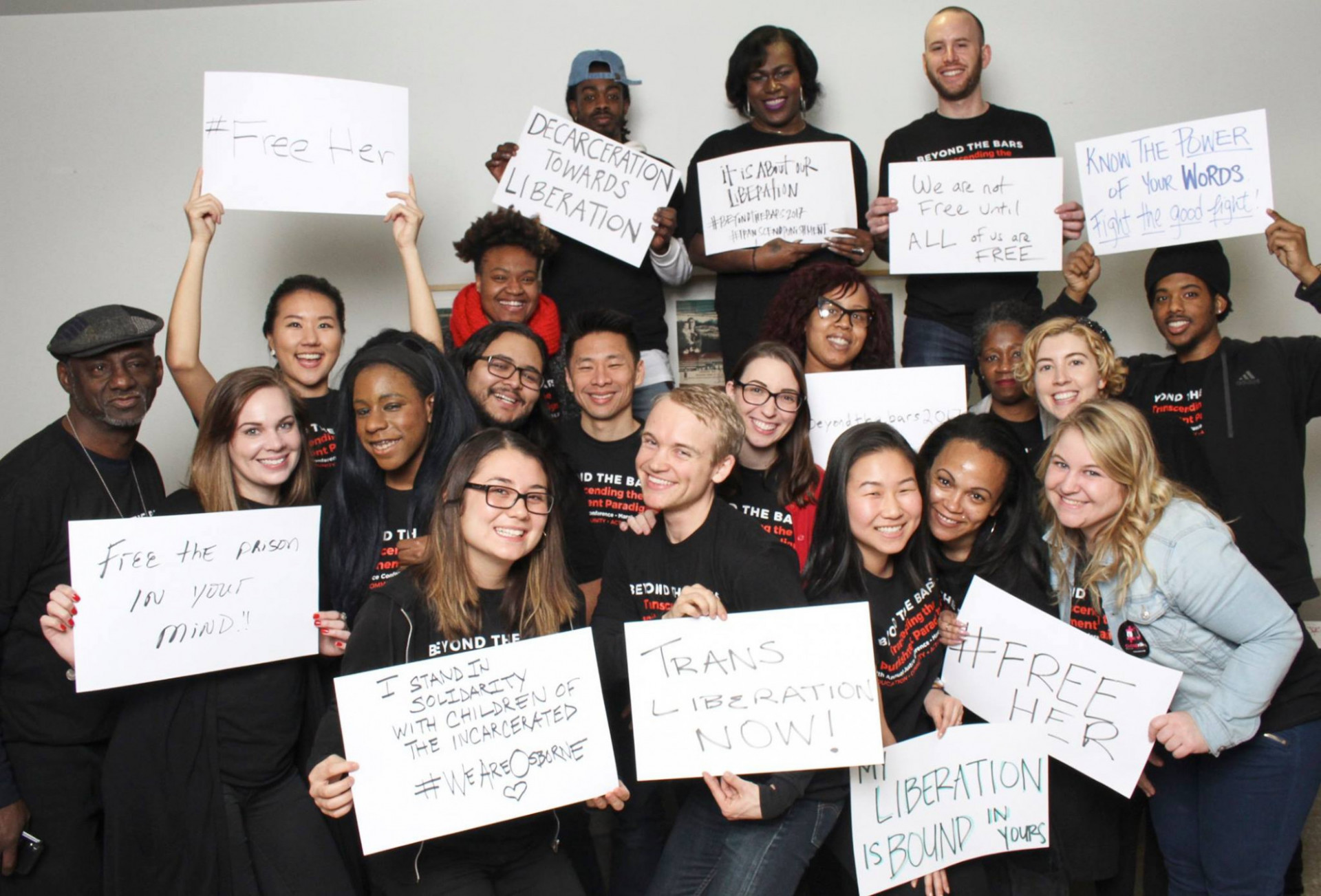 Group photo of people in black shirts holding up white signs