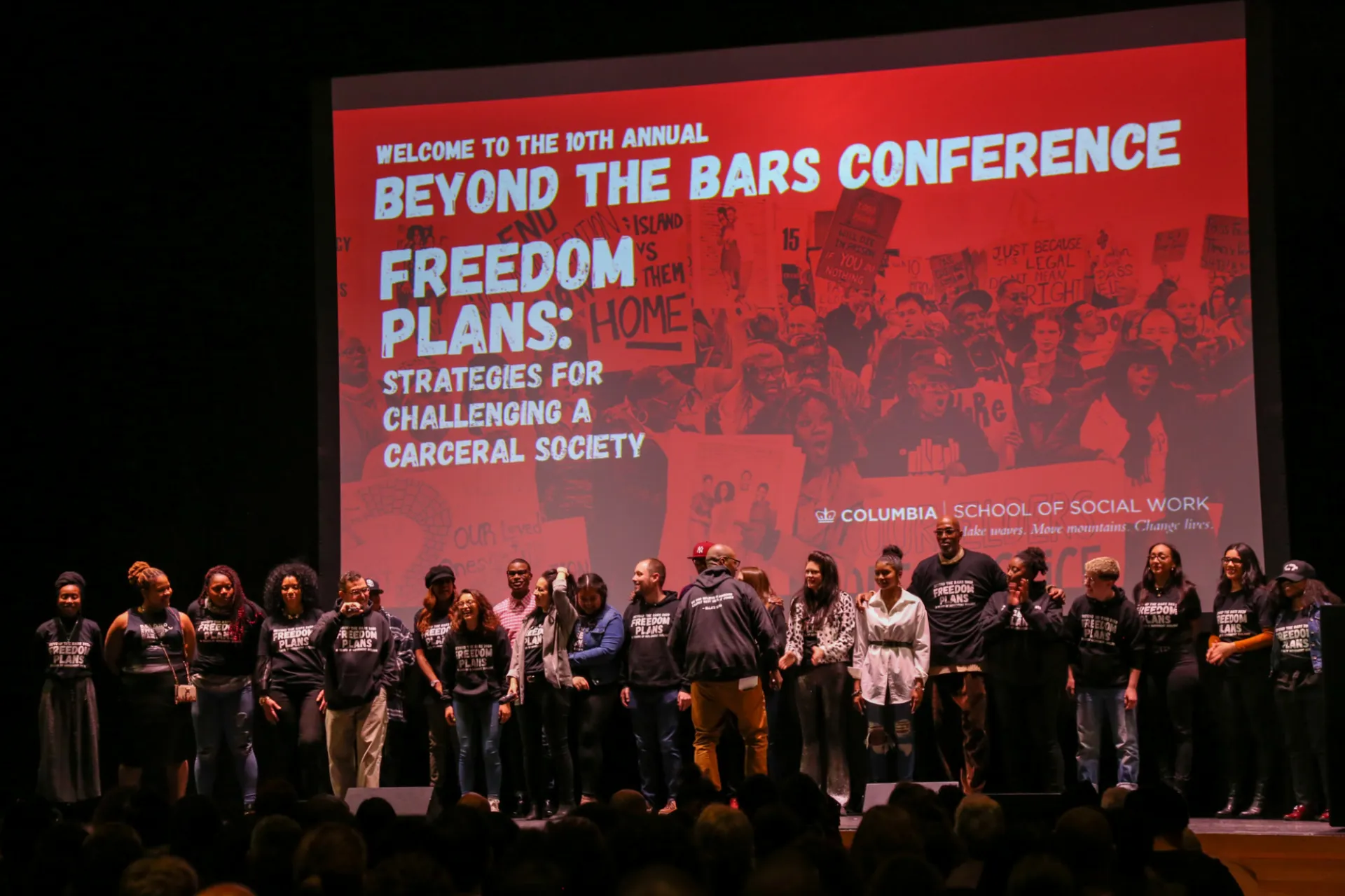 Line of people in black shirts on a stage with a red backdrop that says Welcome to the 10th Annual Beyond the Bars Conference, Freedom Plans: Strategies for Challenging a Carceral Society