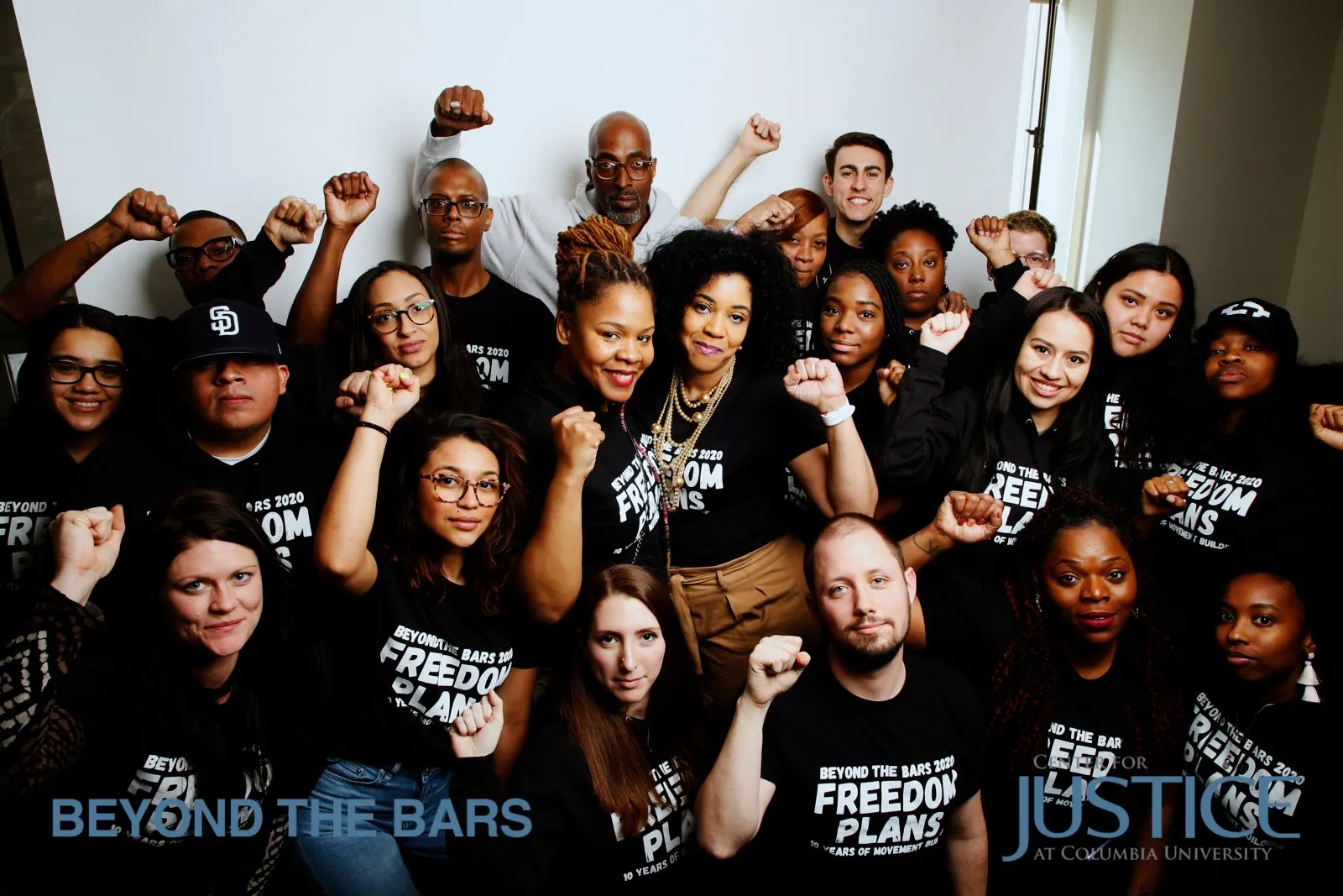 A group photo of people wearing matching black shirts with their fists in the air