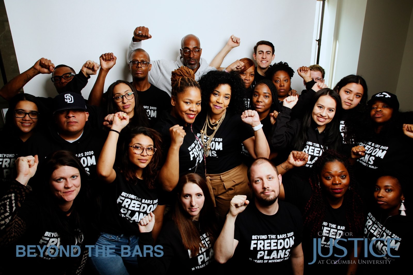 A group photo of people wearing matching black shirts with their fists in the air