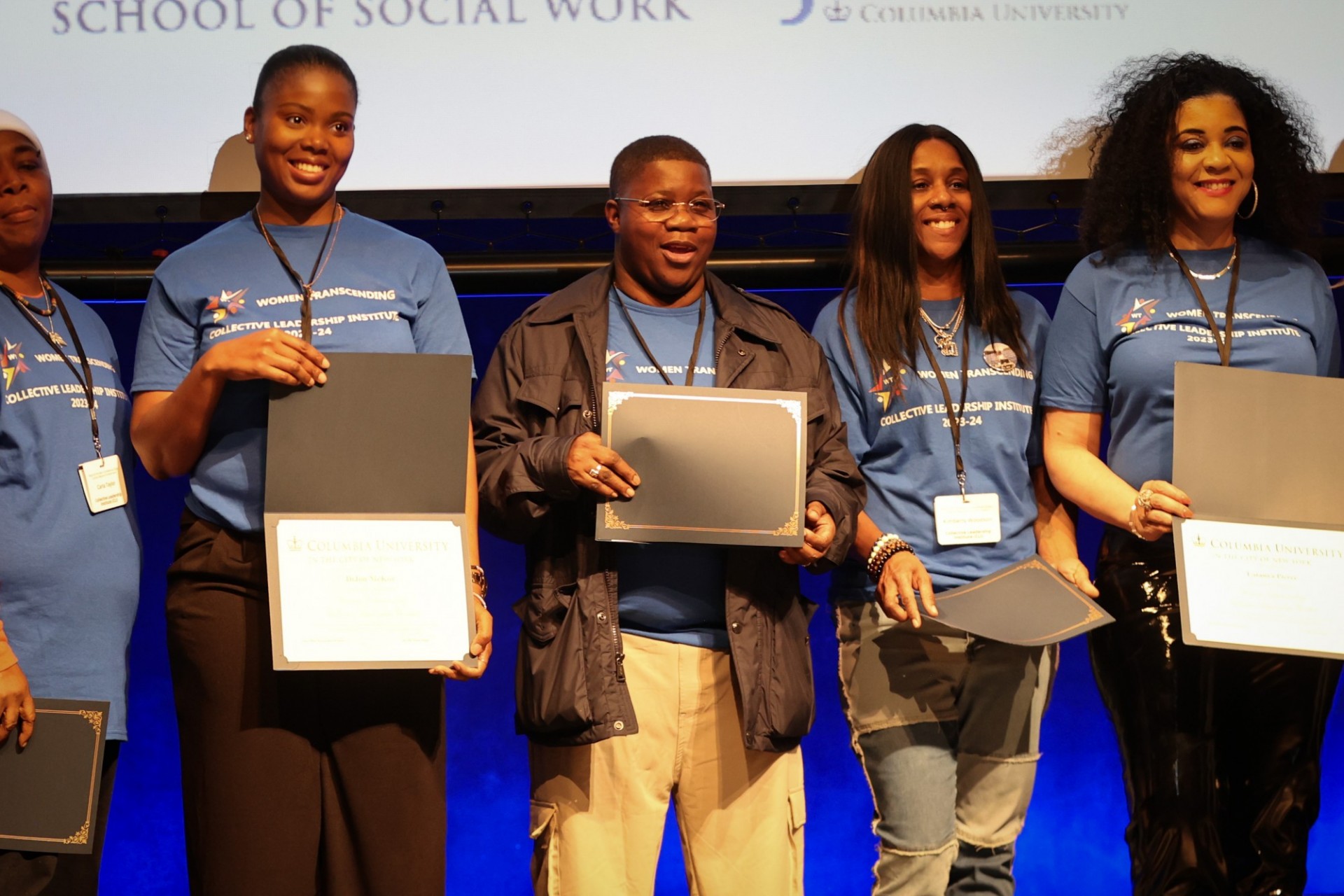 Women on a stage in matching blue shirts holding certificates of program completion