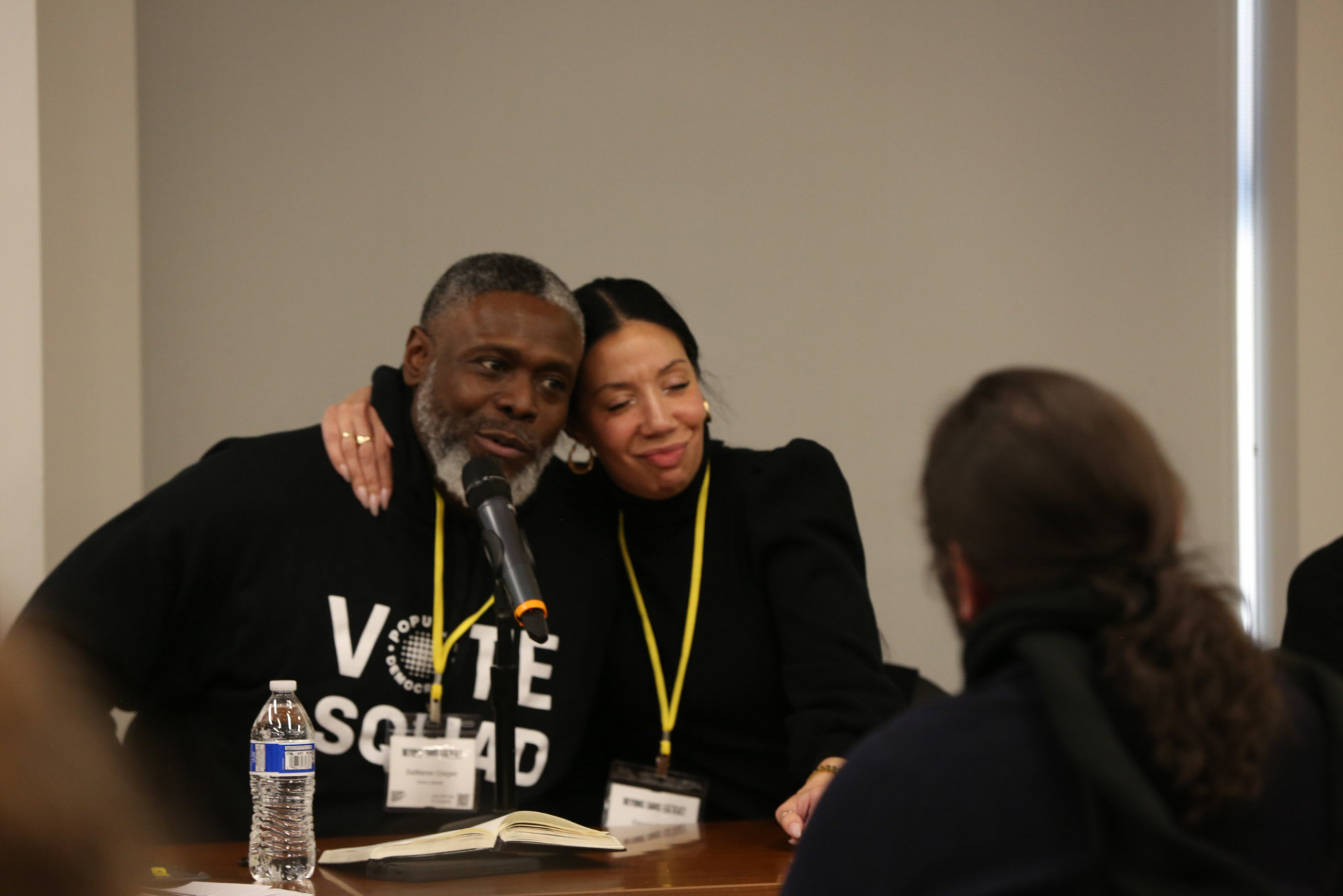 Two panelists sitting at a table with their arm around each other