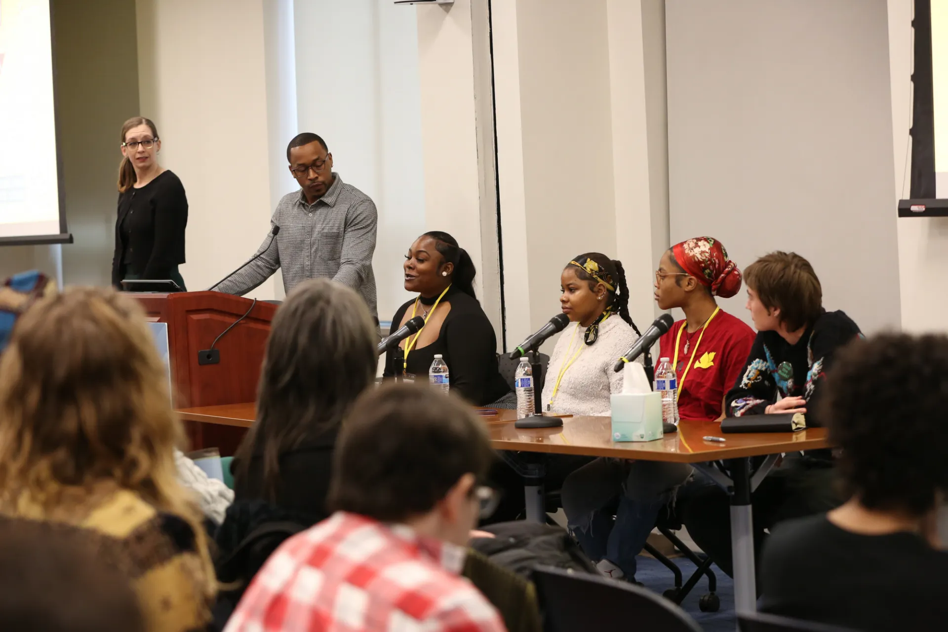 A panel of young speakers sitting at a table in front of microphones and a crowd