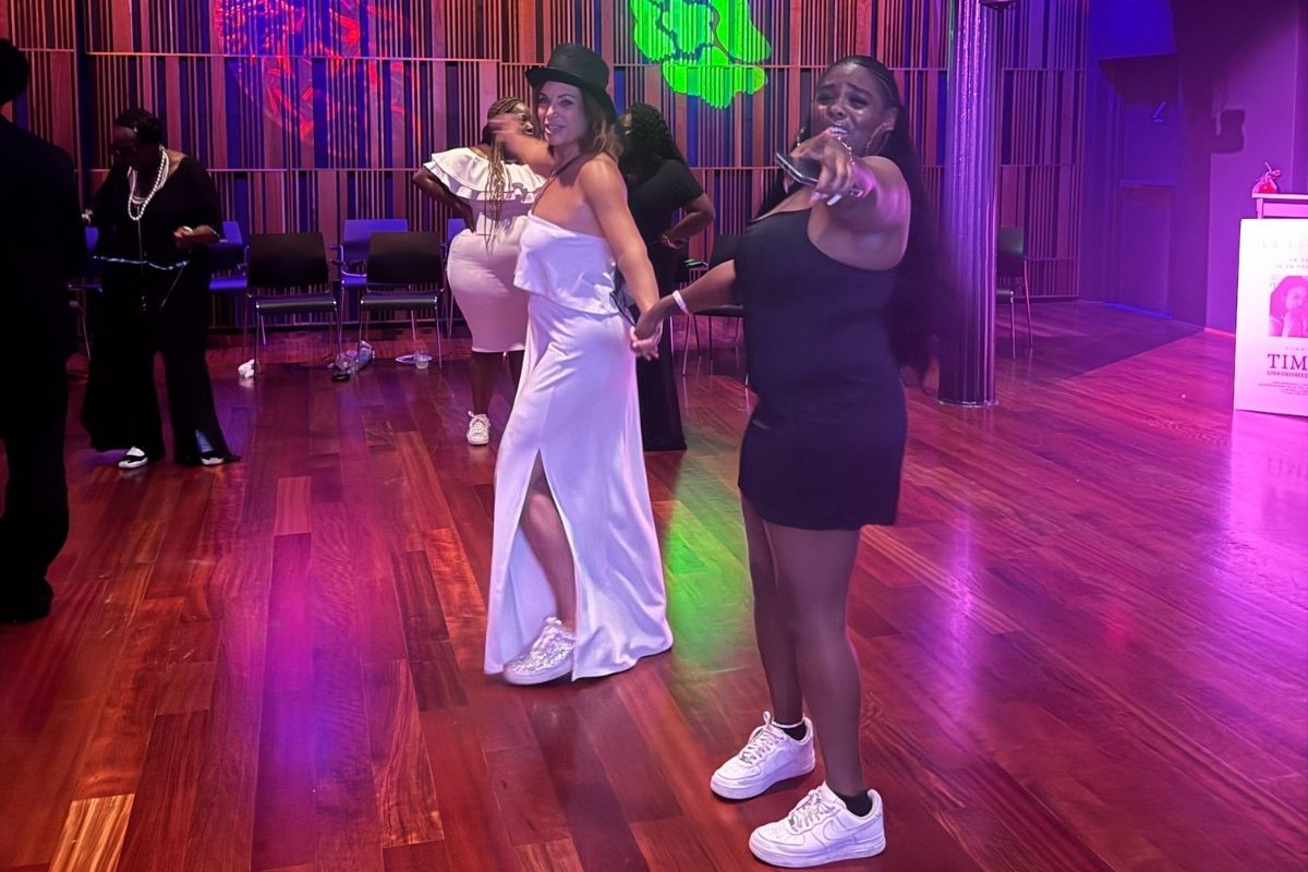Women holding hands on a dance floor and pointing at the camera