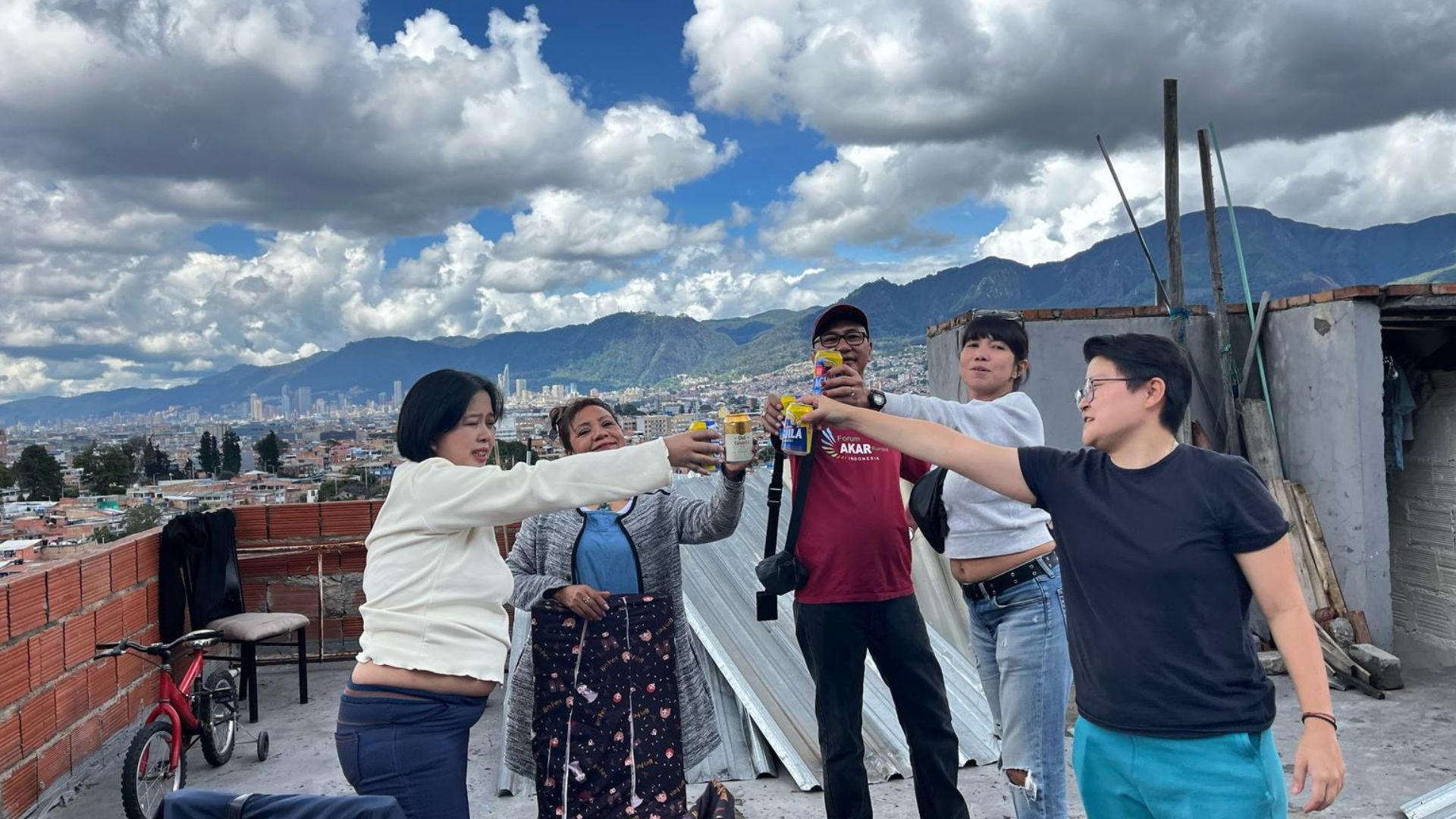 Group of people raising glasses on a rooftop with a city and mountain view in the background