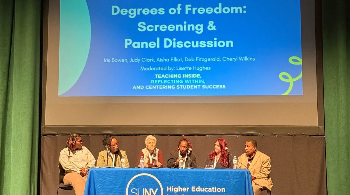 Panel of women on a stage with a screen behind them that says "Degrees of Freedom: Screening & Panel Discussion"