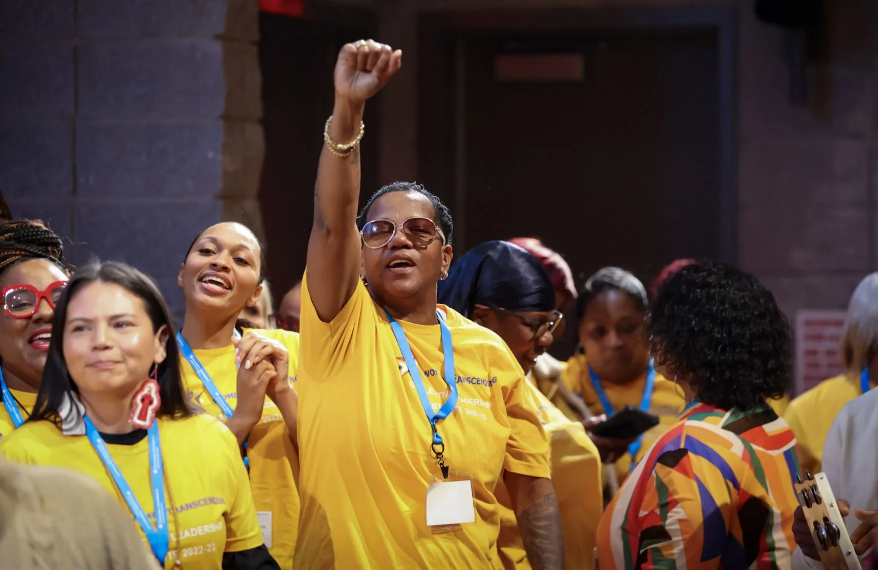 A woman in a yellow shirt with sunglasses on with her fist in the air