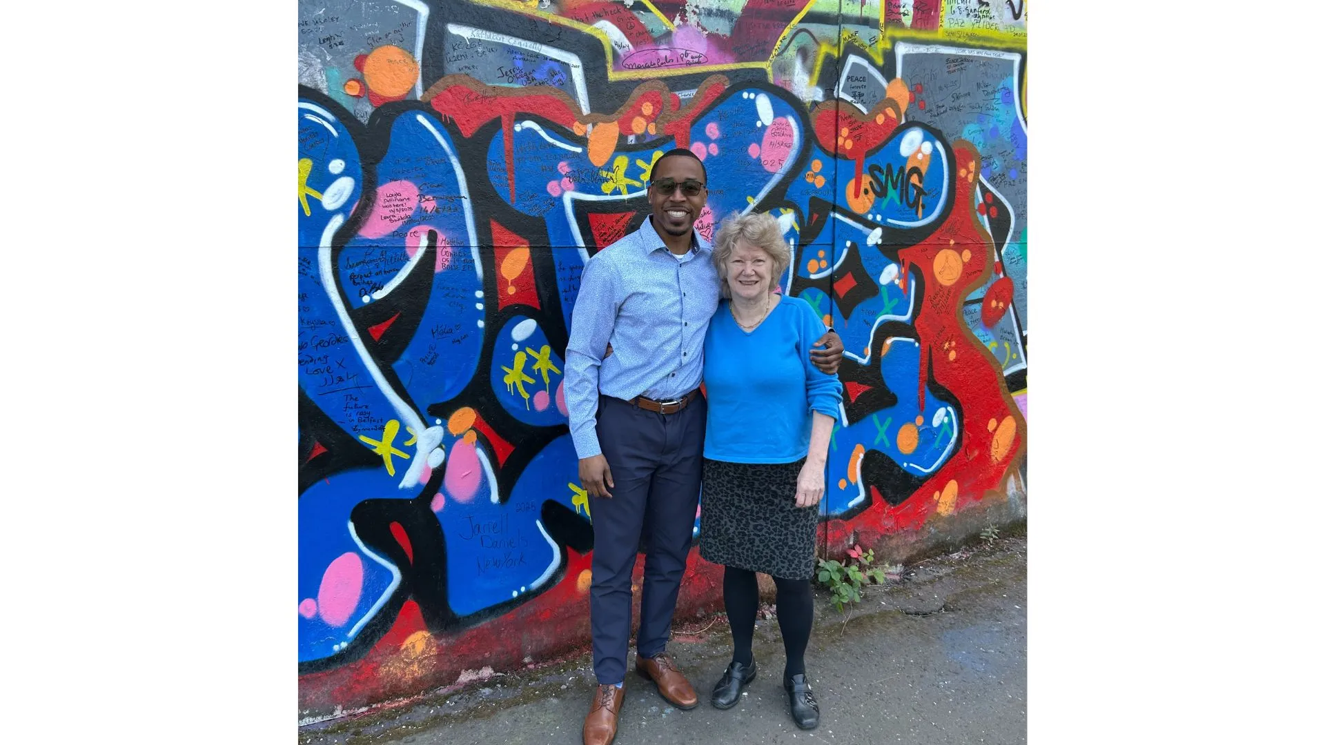 Photo of man and woman posing in front of a graffiti wall