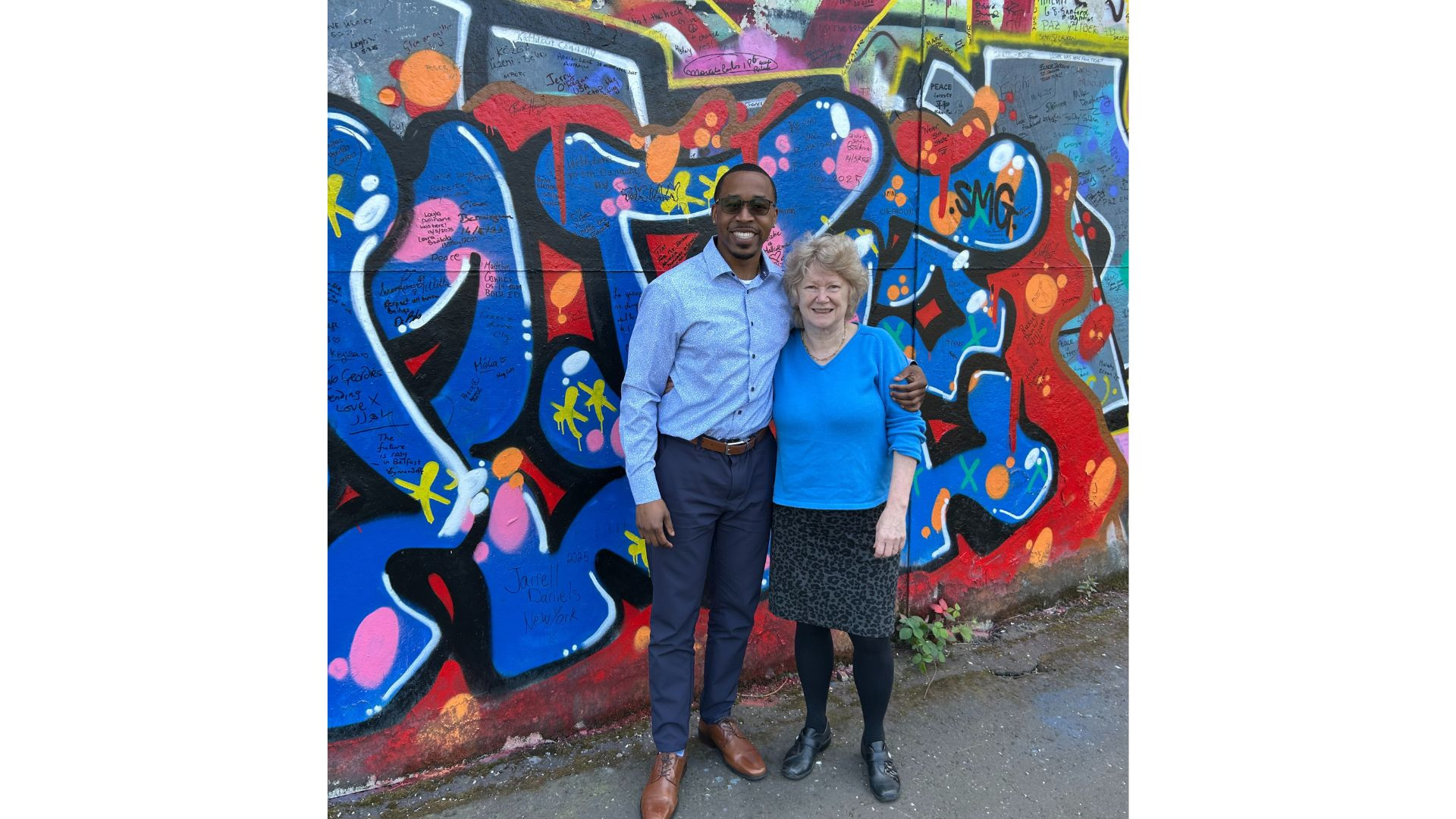 Photo of man and woman posing in front of a graffiti wall