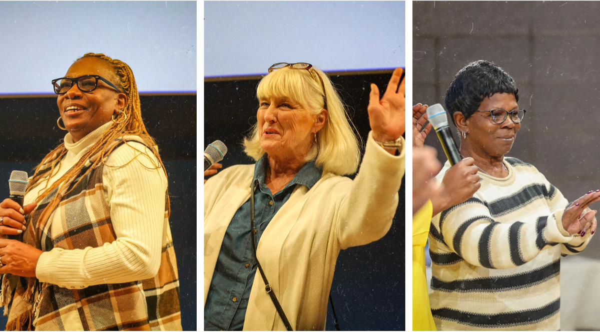 On the left, a Black woman with long brownish blonde hair and glasses smiling as she talks into a microphone on stage; in the middle a white woman with light blonde short hair and glasses on her head, with her hand raised smiling while talking in a microphone; on the right, a Black woman with short dark hair and glasses, waving to someone from the stage