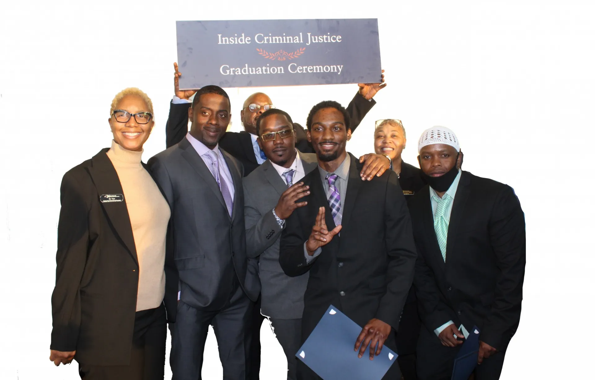 Group photo with a person in the back holding a sign that says "Inside Criminal Justice Graduation Ceremony"