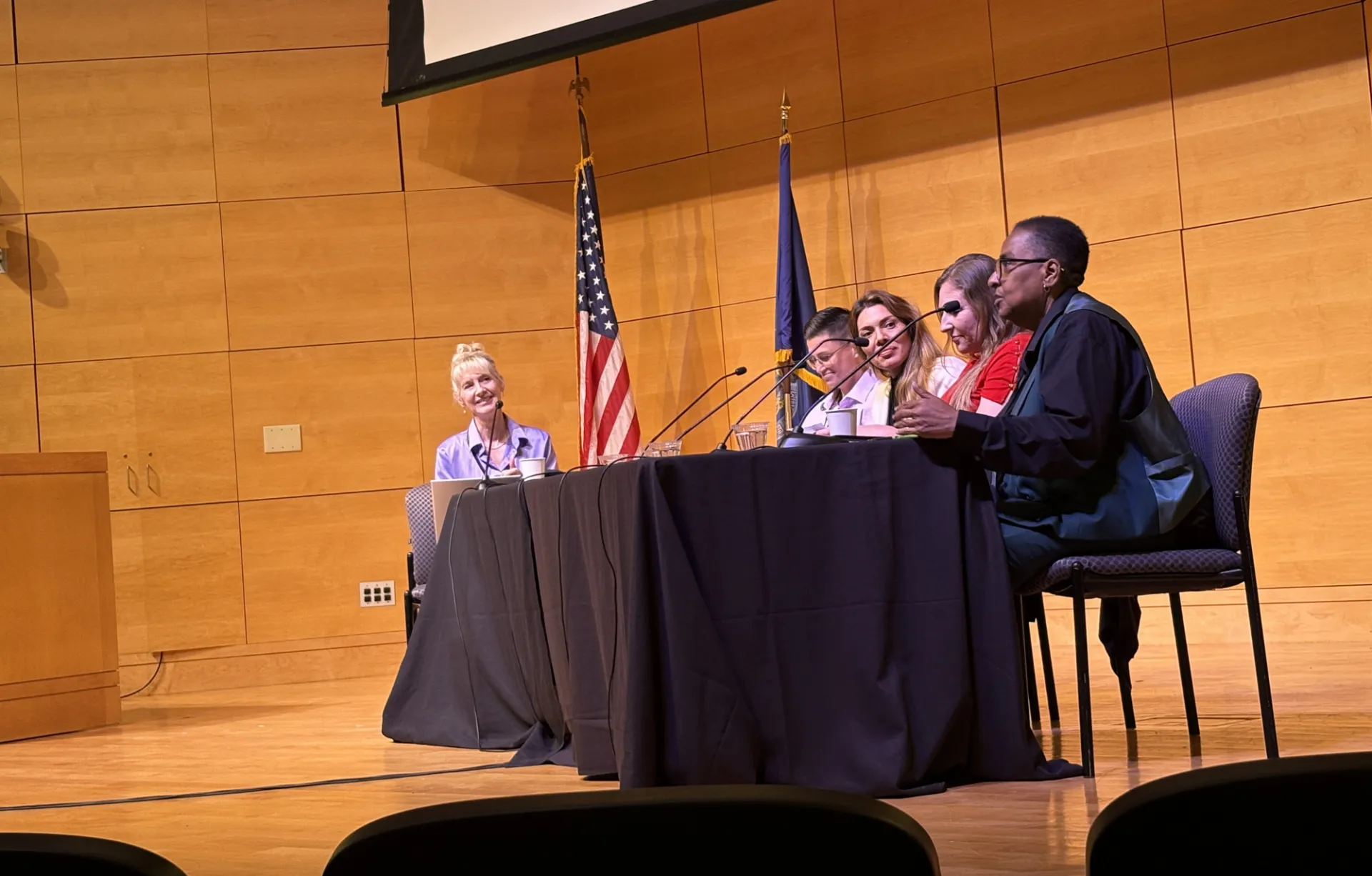 A table on stage with a panel of women in front of microphones