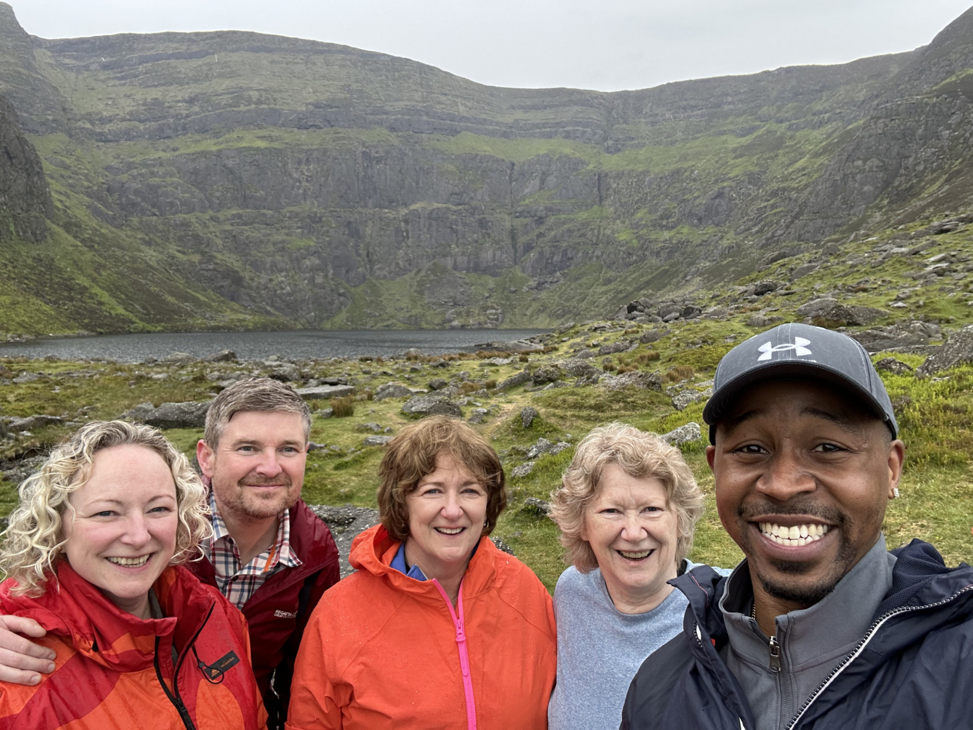 5 people smiling in front of a green mountain