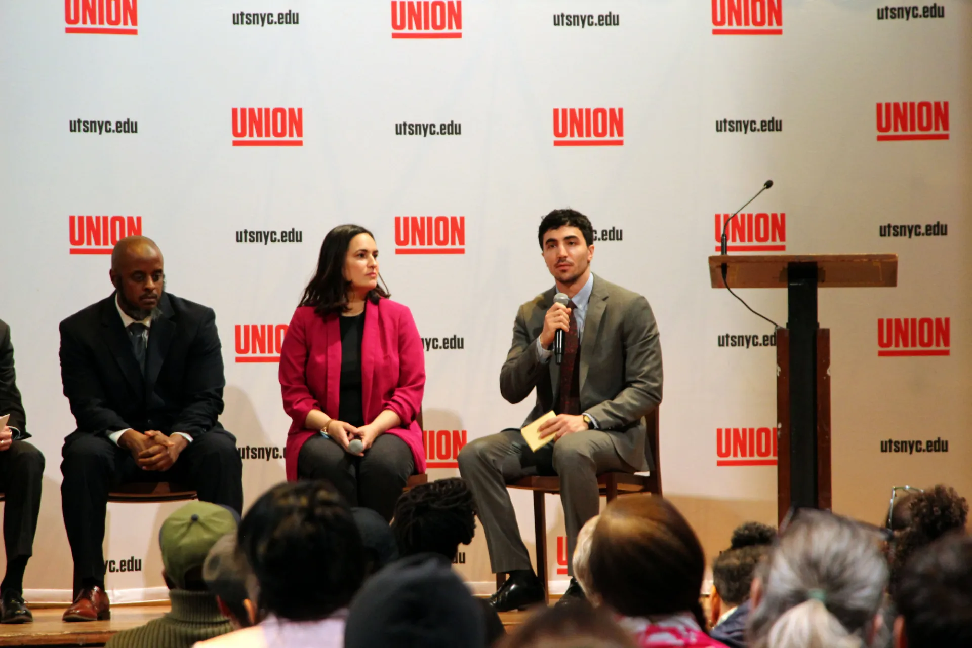 Panel of speakers in front of a step and repeat that says "Union"