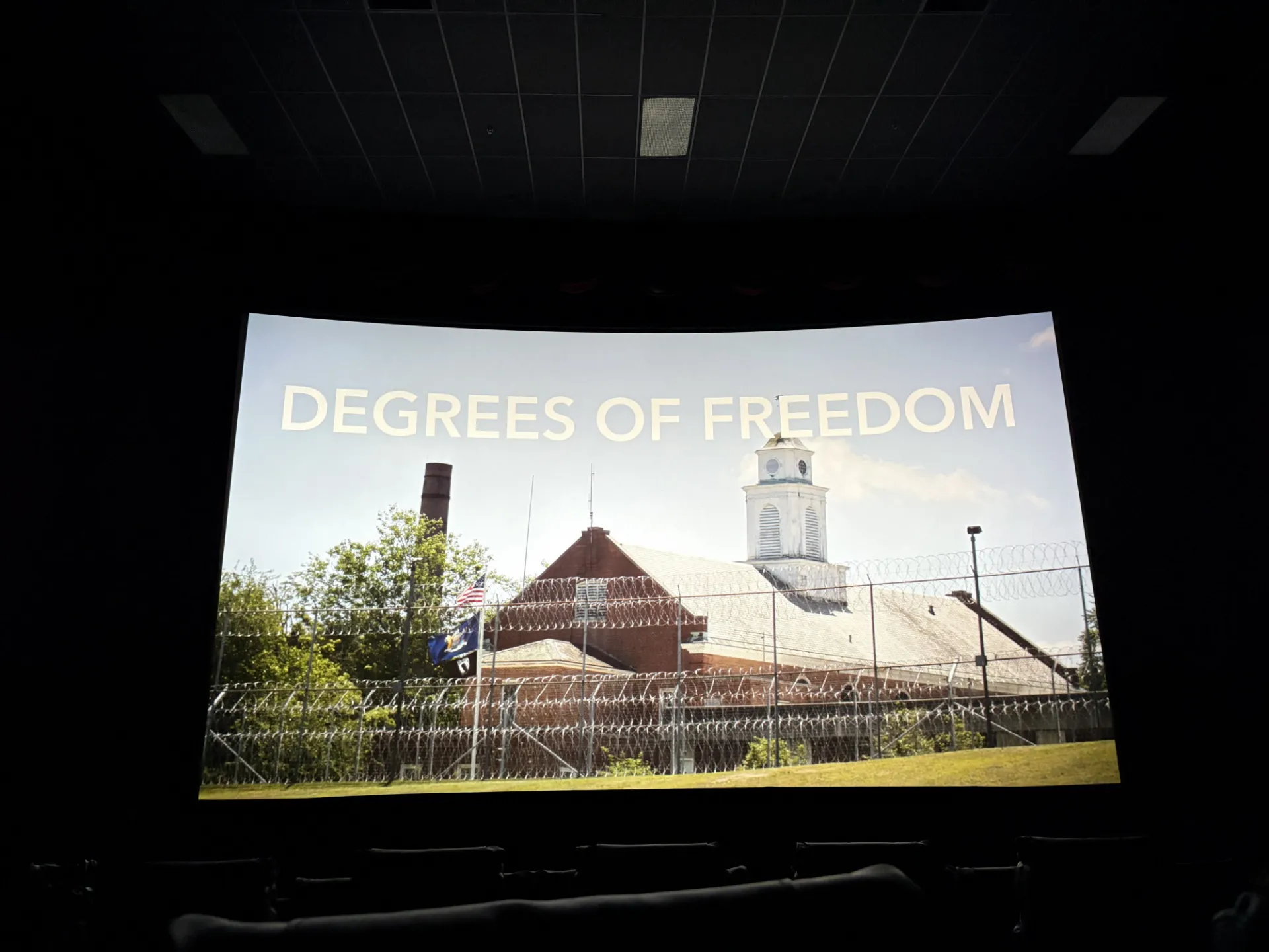 A large movie theatre screen with a photo of a prison and the text Degrees of Freedom