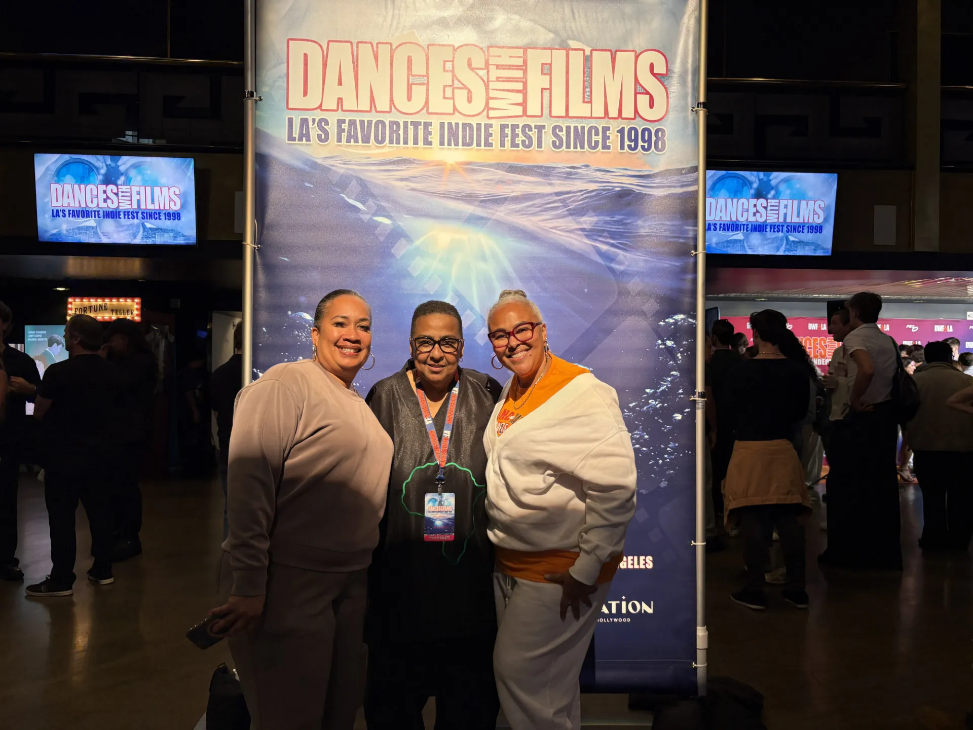 Three women posing in front of a vertical sign that says Dances With Films 