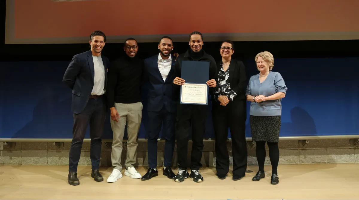 A group of people standing in a row smiling with one in the middle holding up a certificate