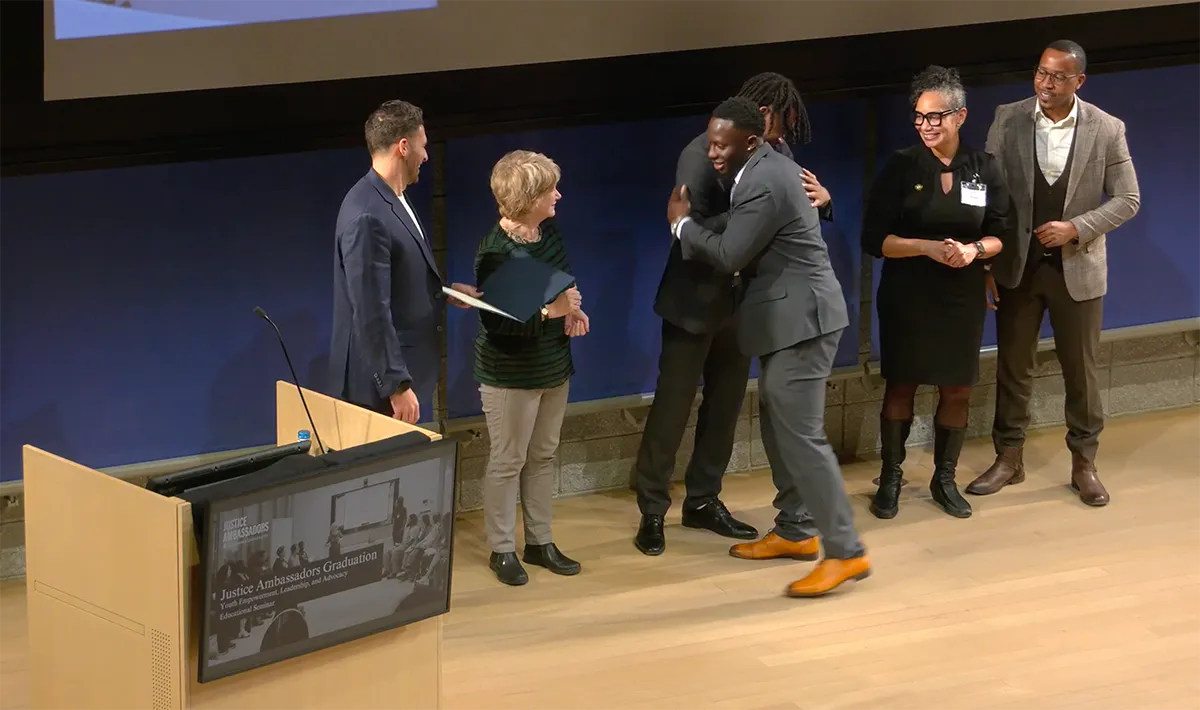 A line of people handing a certificate to a program graduate and congratulating him