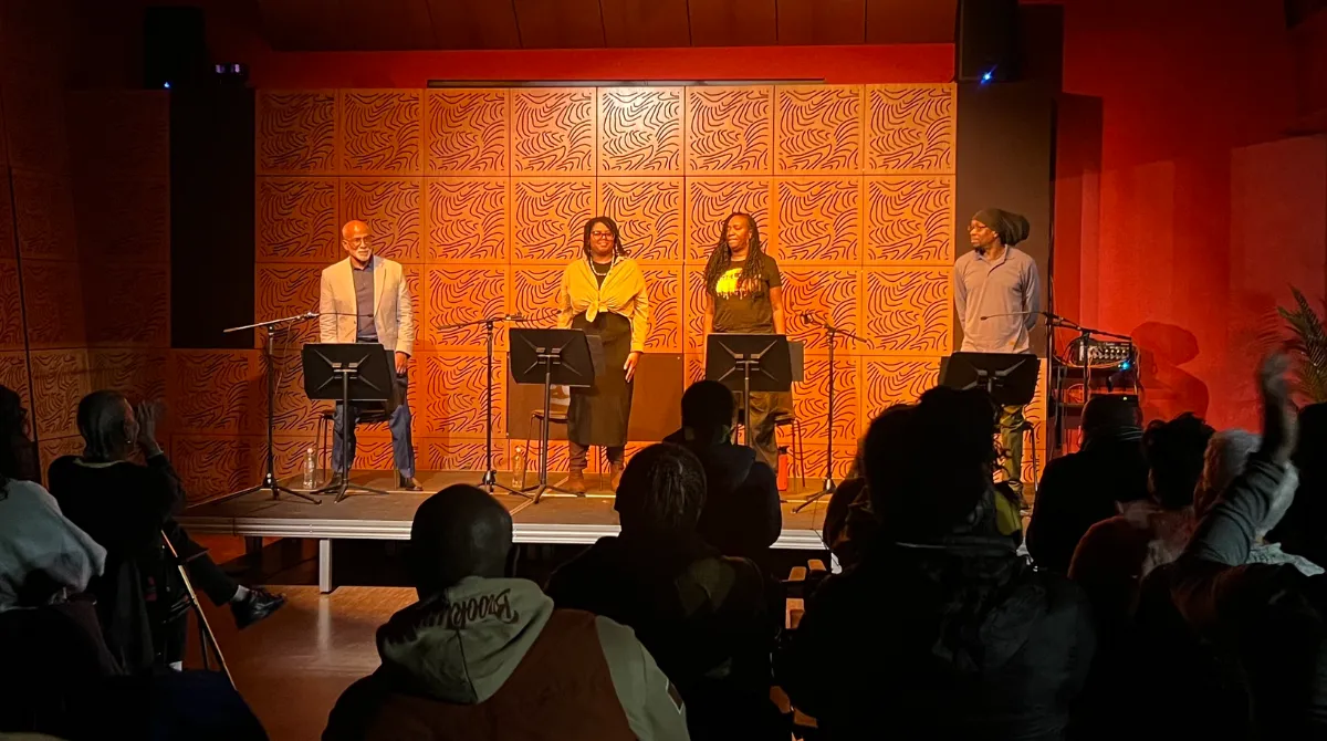 Four people standing on a stage in front of microphones and stands