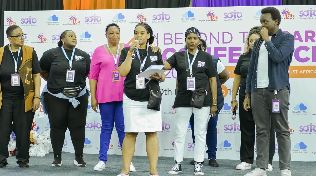 Group of women standing on a stage with a step and repeat banner behind them