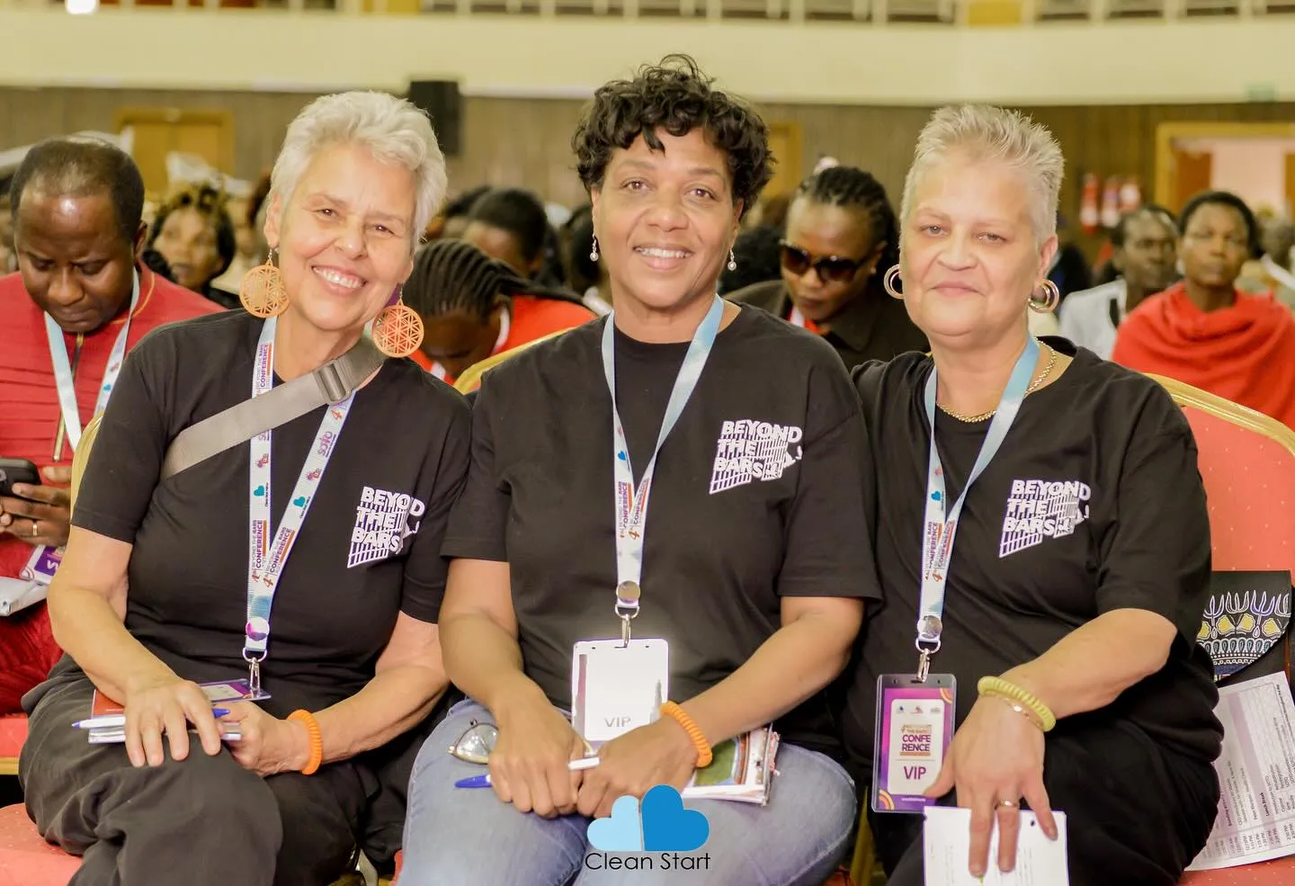 Three women sitting together and smiling for the photo wearing black Beyond the Bars t-shirts