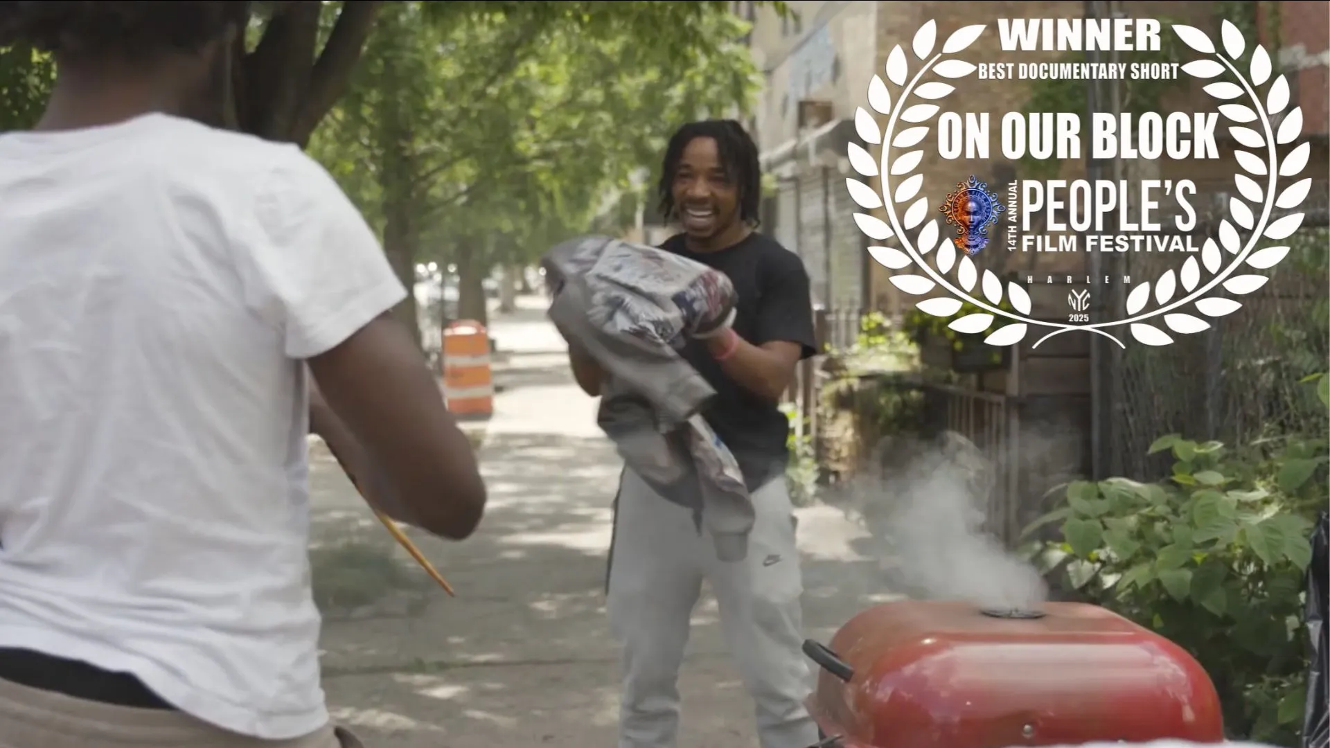 Photo of a young guy holding a jacket in his hands and smiling next to a barbecue. A laurel is overlaid on the image that says "Winner Best Documentary Short On our Block People's Film Festival"