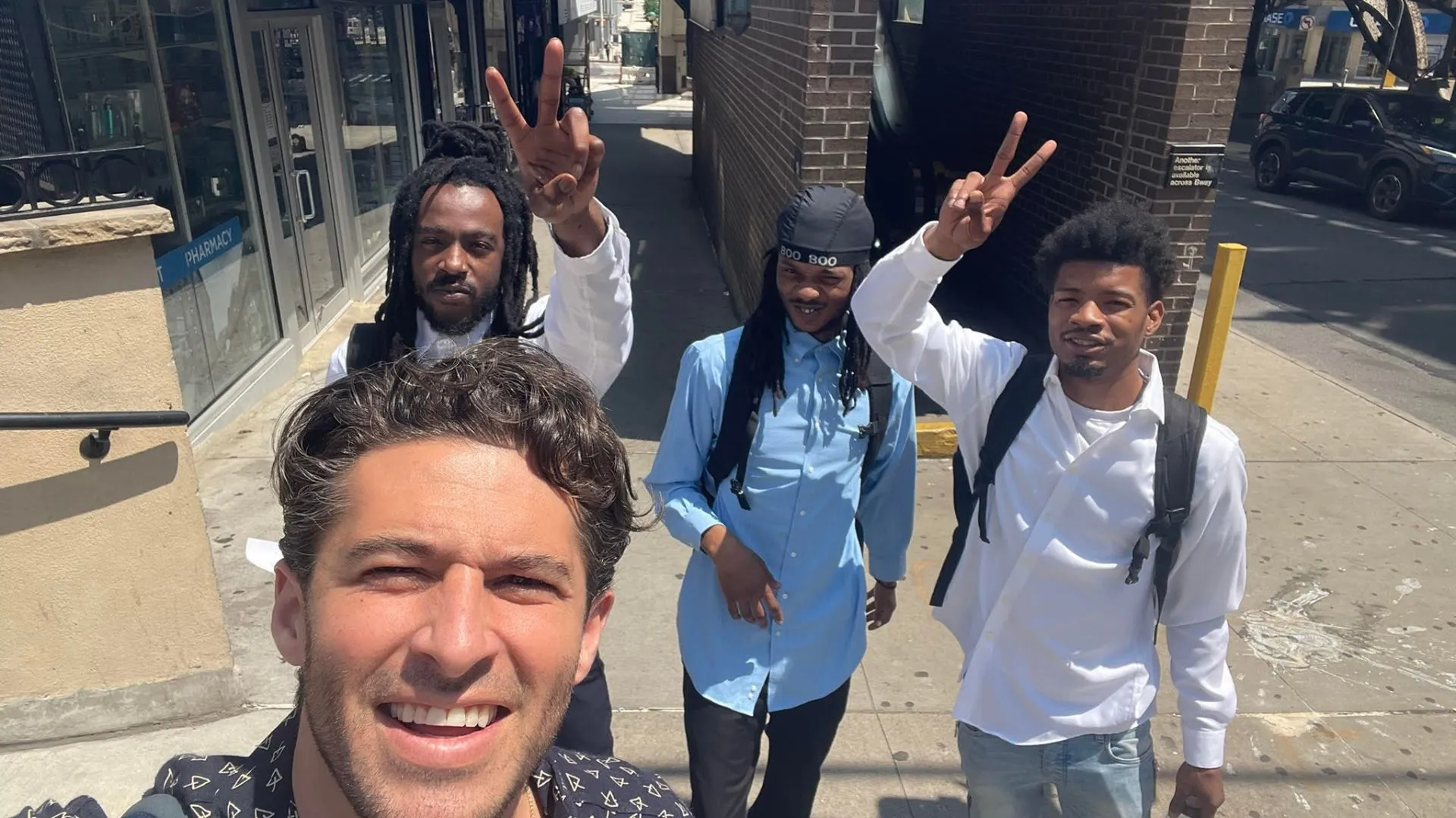 A group selfie of four men with two holding up peace signs 
