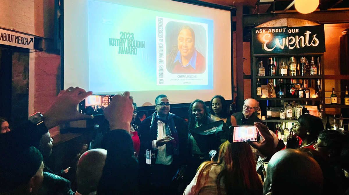 Photo of Cheryl holding an award smiling in front of a screen that says "2023 Kathy Boudin Award"