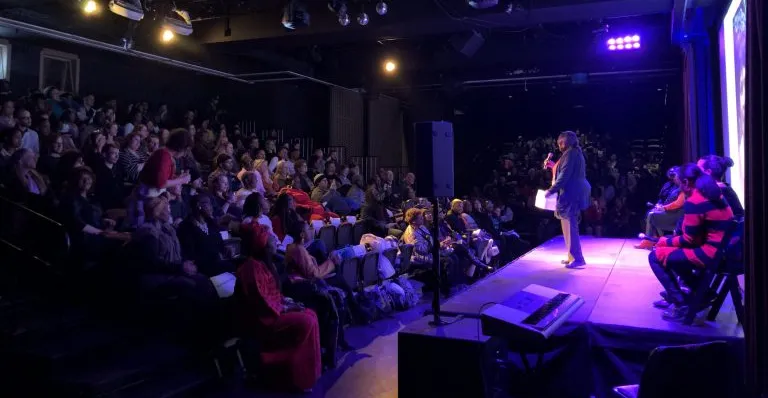Cheryl Wilkins appears on stage addressing Beyond the Bars conference participants in a theater.
