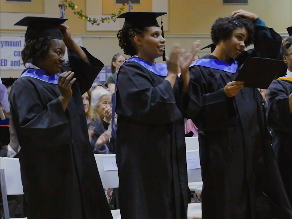 women in black graduation caps and gowns standing and clapping