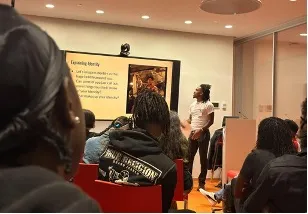 A young man looking at a powerpoint presentation presenting to a group of people 