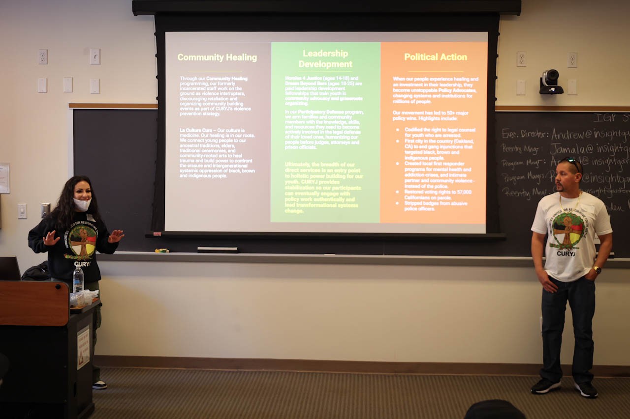 Two workshop leaders standing in front of a classroom with a powerpoint slide on the screen