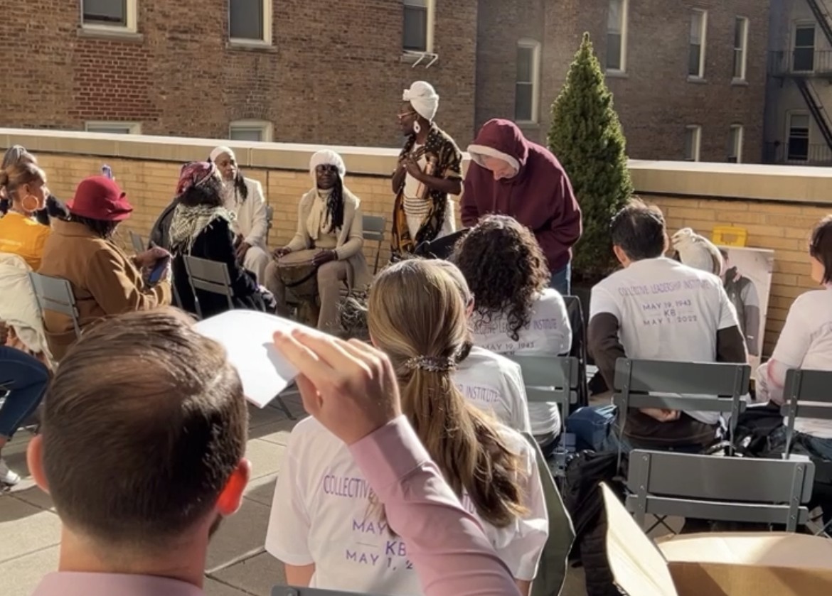 A group of people sitting in chairs outside around a tree