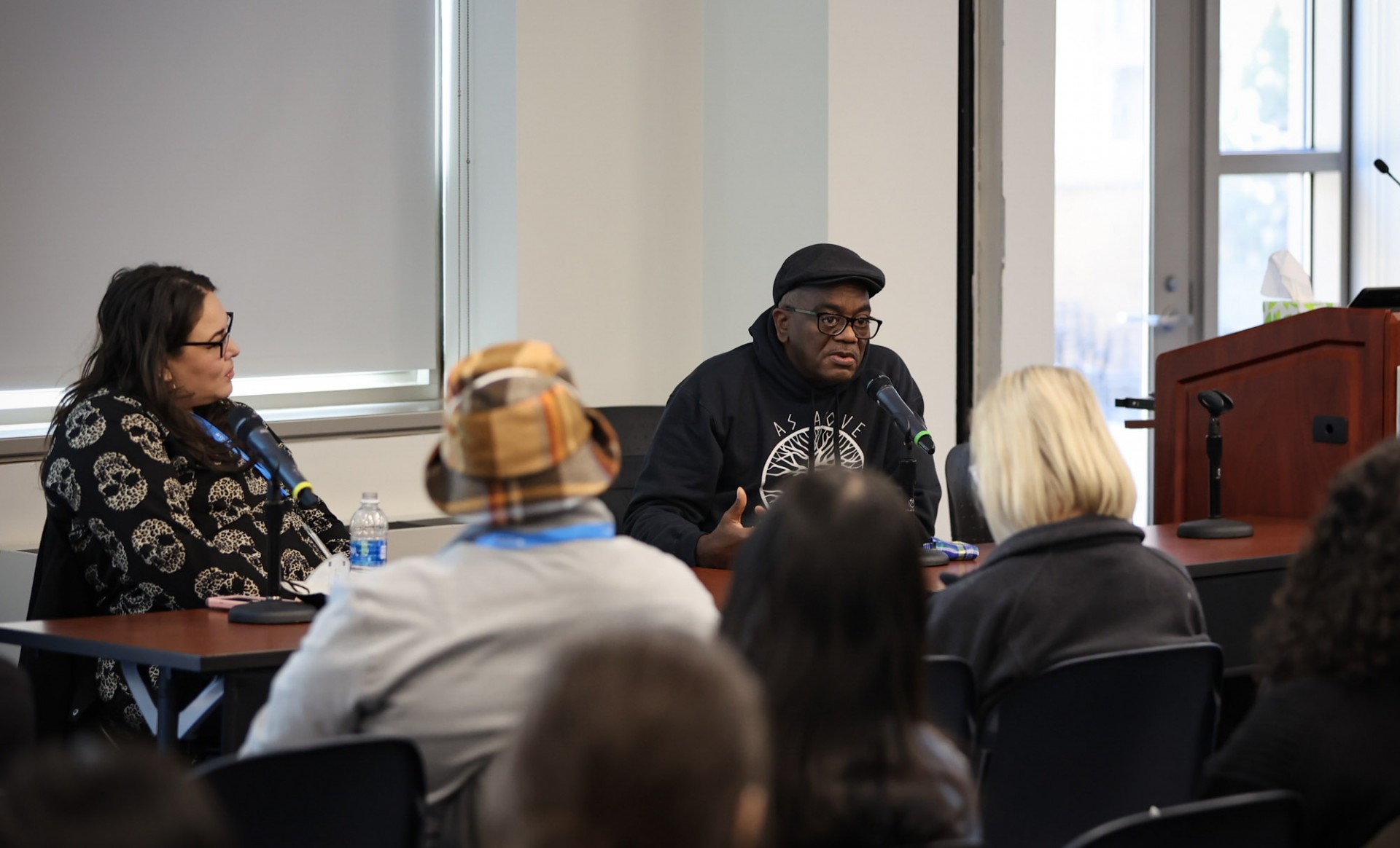 Man and a woman sitting at a table in front of an audience in a classroom 