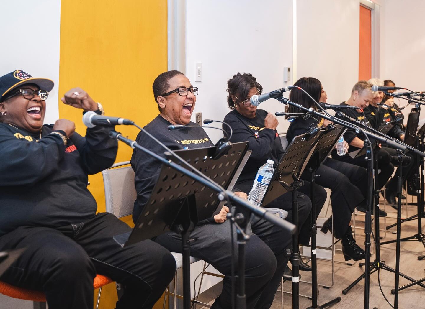 A row of women sitting in chairs behind microphones and stands, laughing