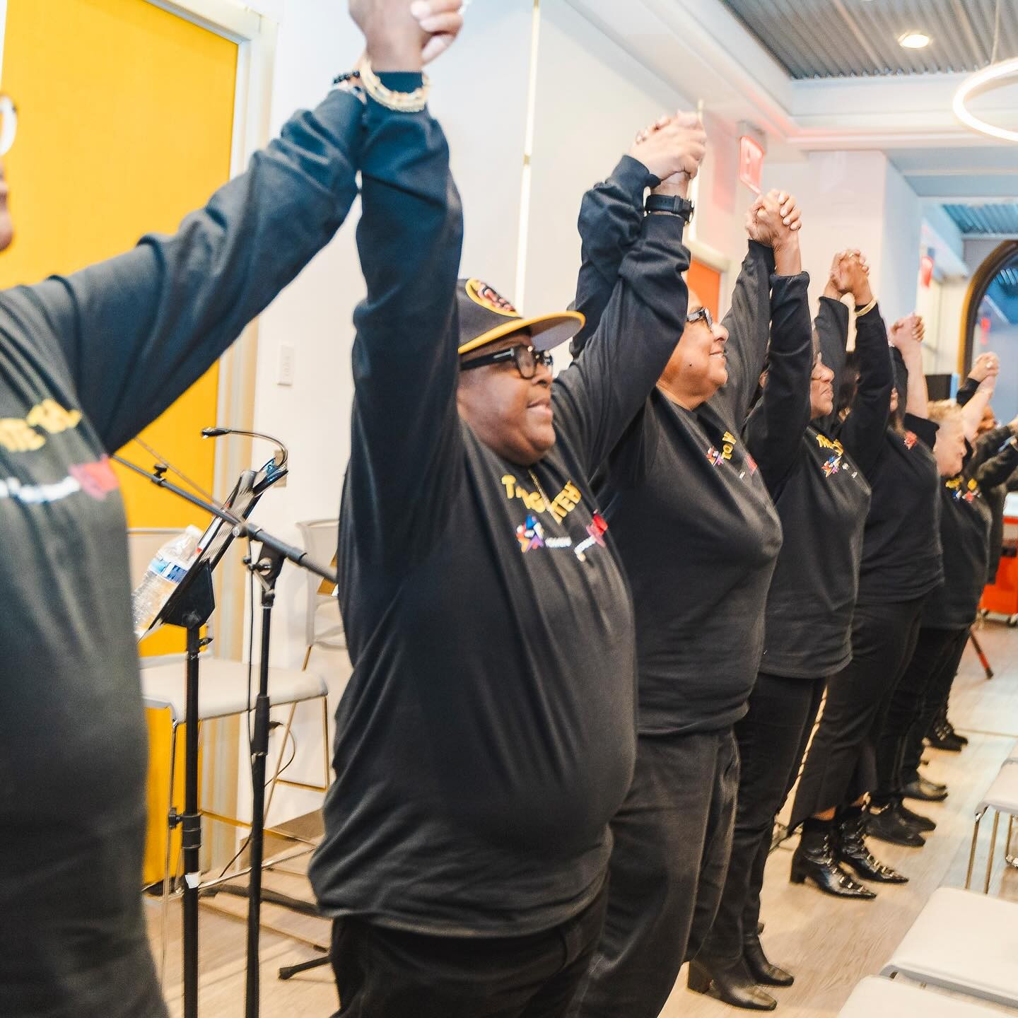 Women in a row in black shirts holding up raised hands before taking a bow