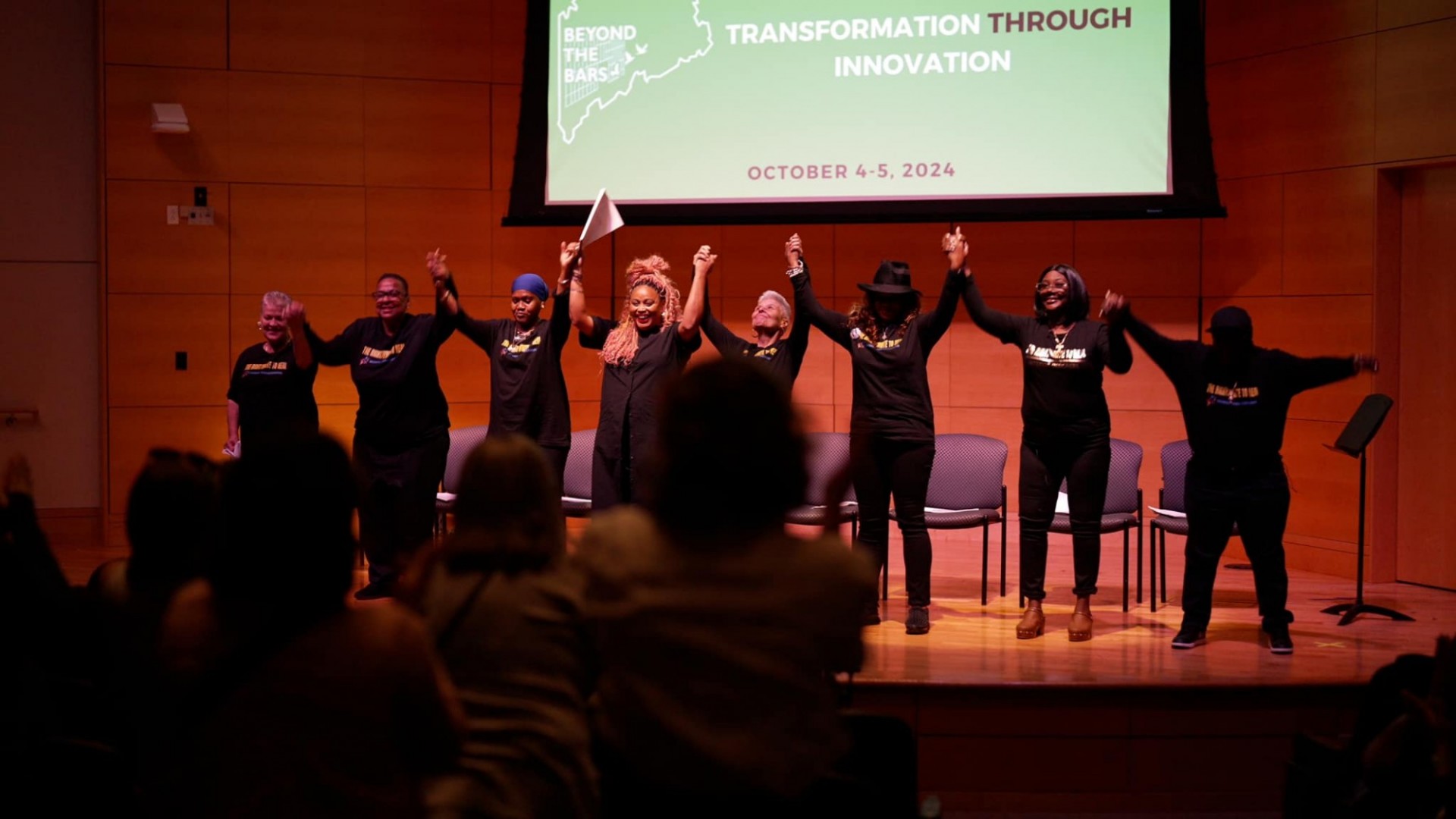 Women in black shirts holding hands while raising them together to take a bow after a performance 